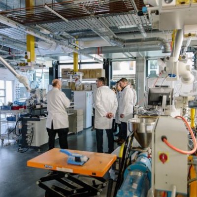 A group of people in white coats look at machinery inside a high-tech laboratory
